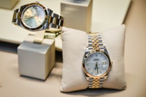 picture of jewelry: 2 gold watches, one on a display stand, and on on a display pillow. 