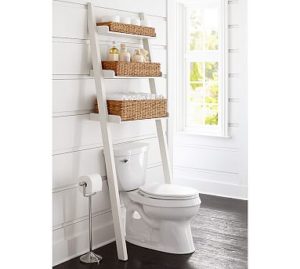white ladder shelf leaning backwards over a toilet with wicker baskets on the shelves
