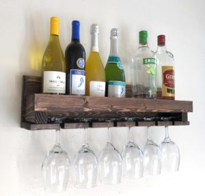 Wine Rack, Glass Holder by WoodymoodLLC from Etsy dark wood shelf mounted to wall with wine and liquor bottles and wine-glass holding slots, wine glasses hanging upside down