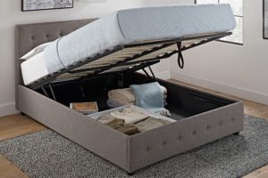 large grey upholstered platform bed with platform raising up to reveal storage within the bottom 