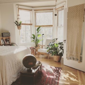 Image of 3 windows in a beige-colored bedroom decorated in a scandinavian style with 3 large green plants.